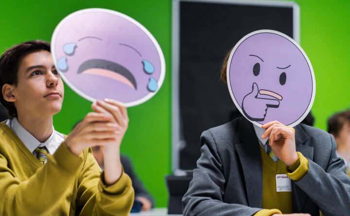 Students in a classroom holding emoji masks in front of their faces.